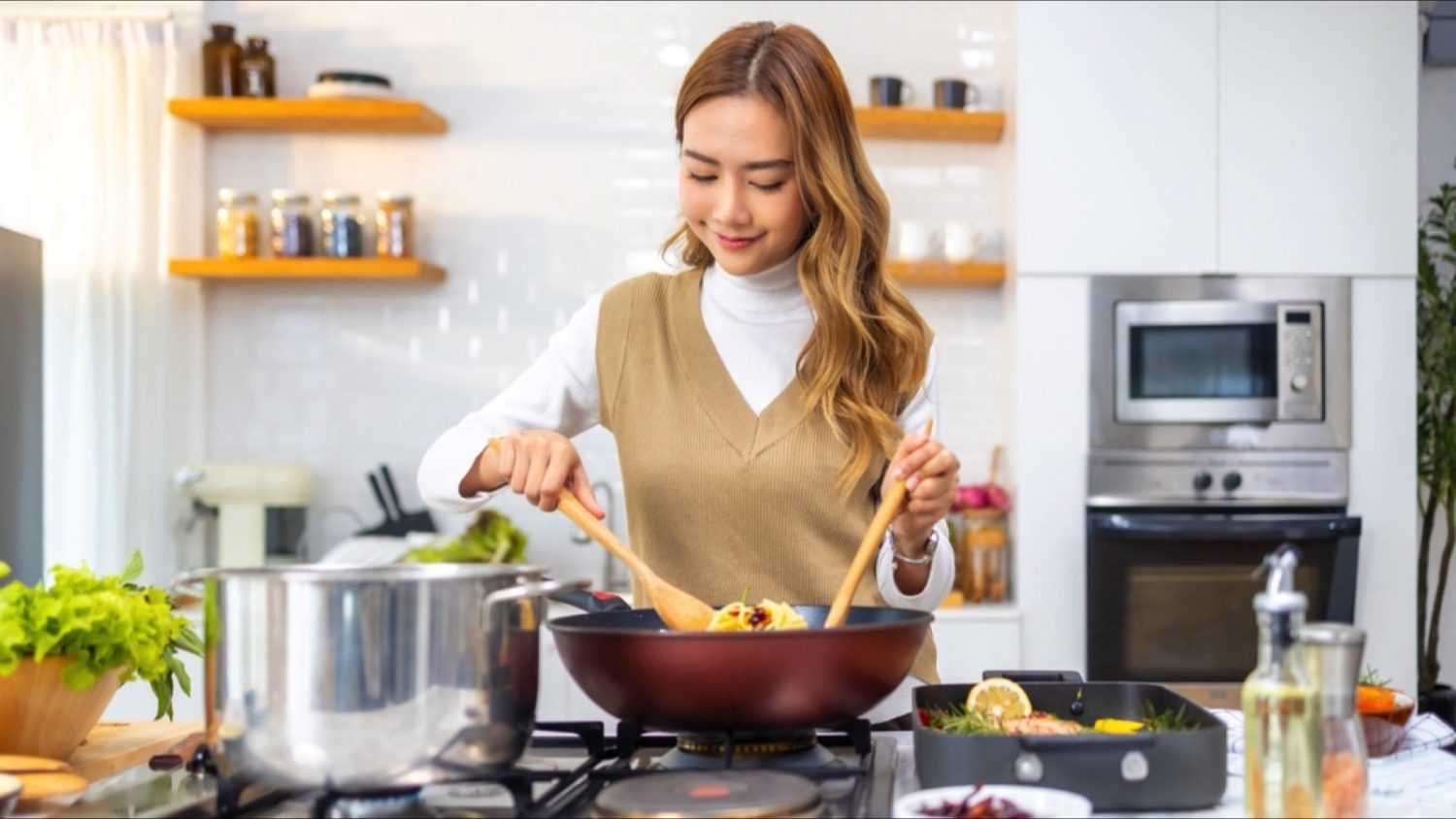 A woman skillfully cooks in a kitchen with enjoy home organization, focused on a pan as she prepares a delicious meal.