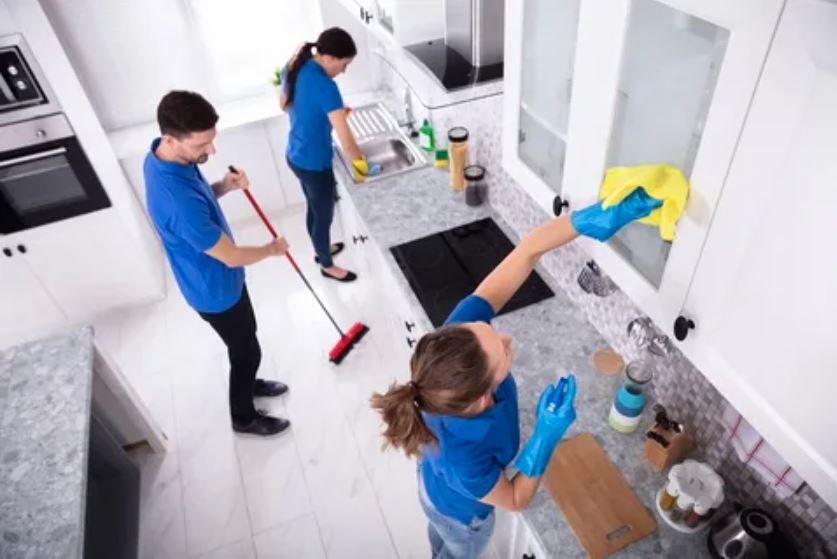 Two individuals diligently cleaning a kitchen using a mop and a dustpan, ensuring a tidy and hygienic environment.